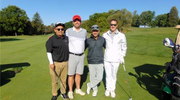 A foursome poses against the green course and blue sky.
