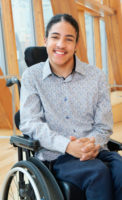 Dante in a buttoned shirt smiling sitting in his wheelchair