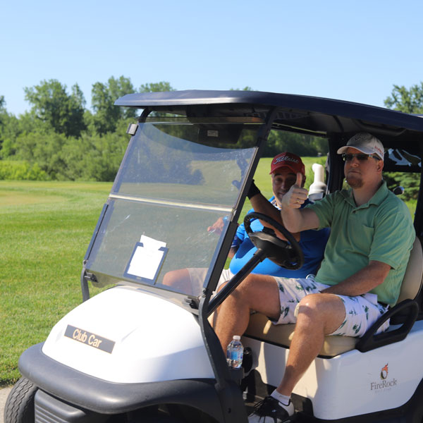 Two golfers wave from a golf cart