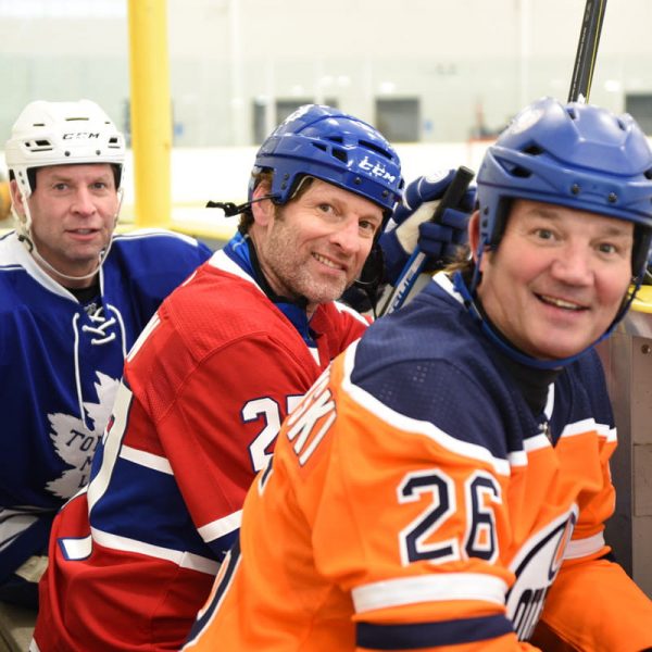 Three NHL Alumni players sitting on a bench at the rink