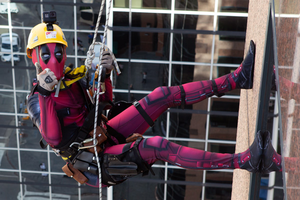 A person in a Deadpool costume gives a thumbs up while rappelling down a buidling.