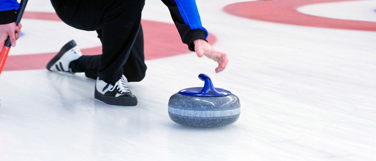 A man hurls a blue curling stone