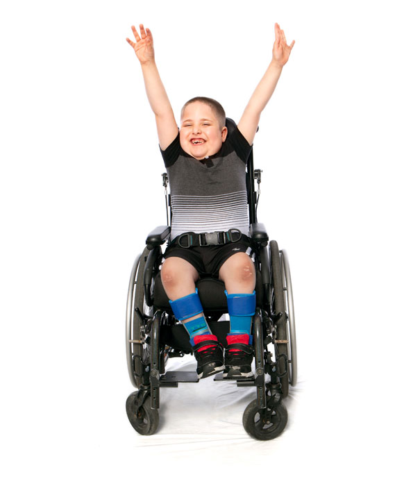 Picture of Kyle in a wheelchair holding his hands in the air while smiling.