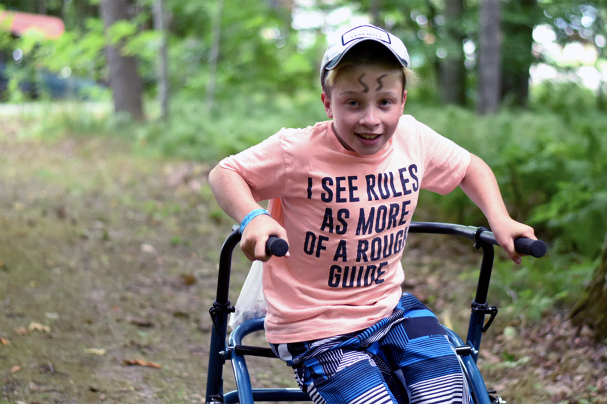 A boy in a walker with a t-shirt that reads I see rules as more of a rough guide.