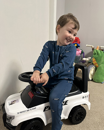 Wesley smiling and sitting on a push car.
