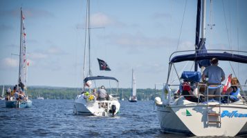 Three large boats sail away in a line under a blue sky